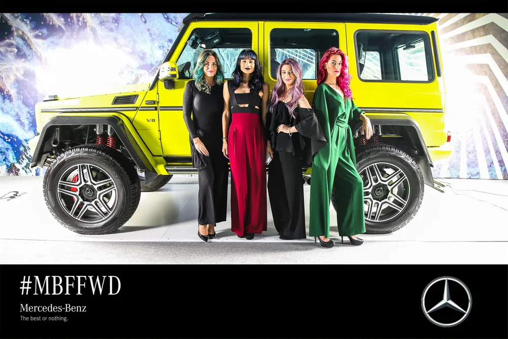 Four guests posing beside a yellow Mercedes-Benz in a branded photo frame.